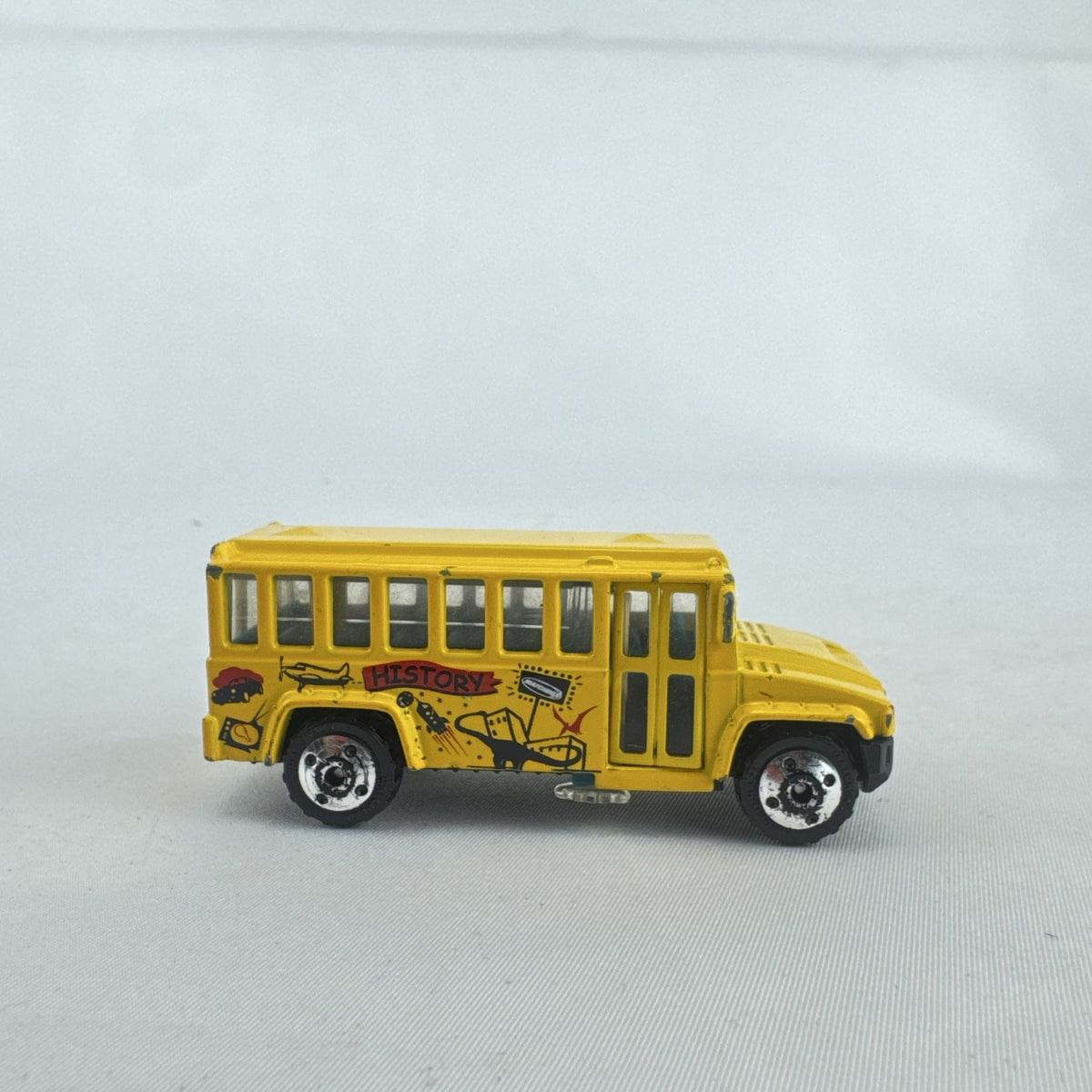 Matchbox 1:64 scale yellow diecast school bus with History dinosaur and rocket graphics