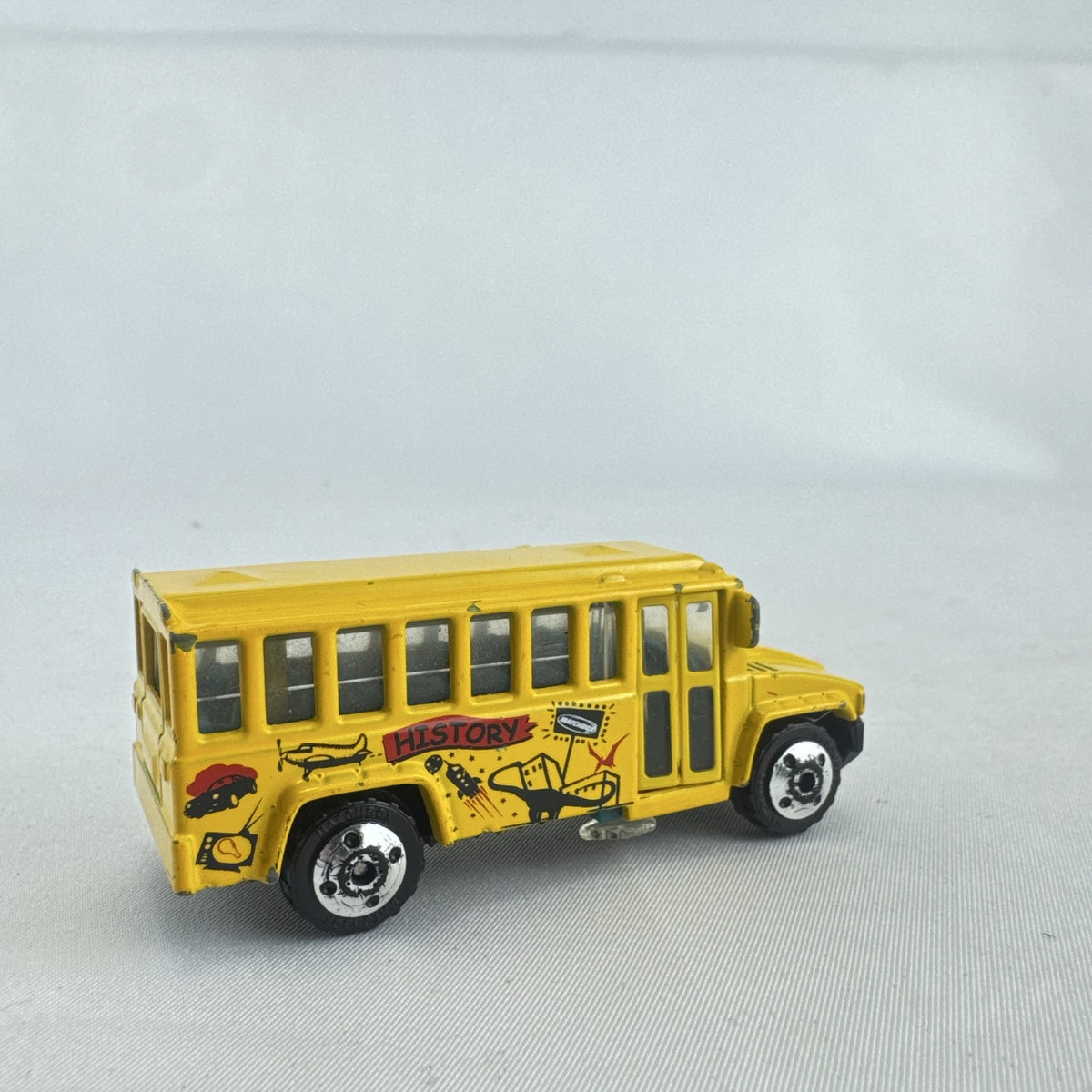 Matchbox 1:64 scale yellow diecast school bus with History dinosaur and rocket graphics